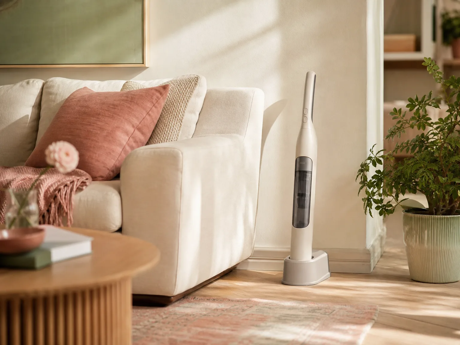 A slim cordless handheld vacuum resting upright on a low charging dock beside a cream sofa in a lived-in living room