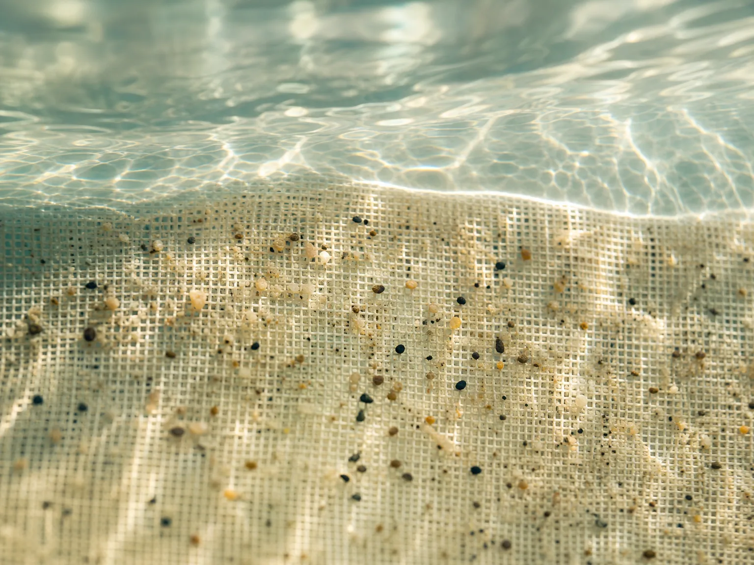 Close-up of fine mesh filtering debris from clear pool water, shallow depth of field with sunlight refracting through the water surface