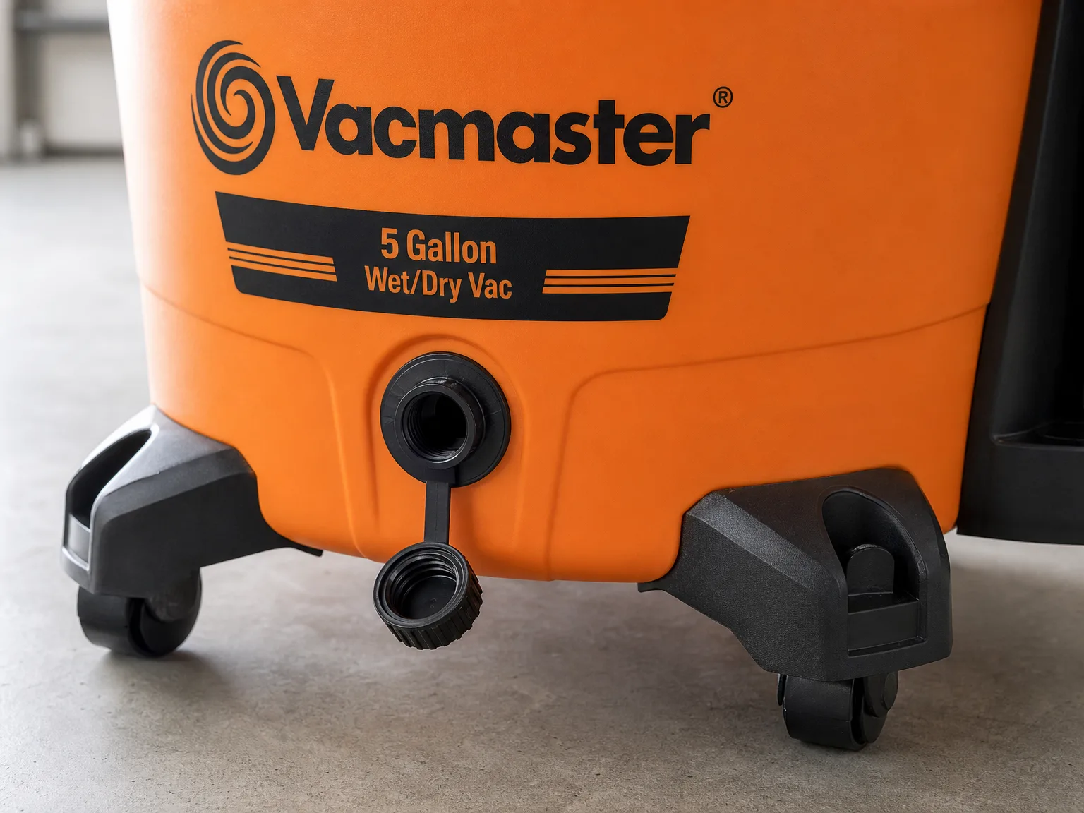 Close up of the Vacmaster drain plug and plastic canister body on a garage floor