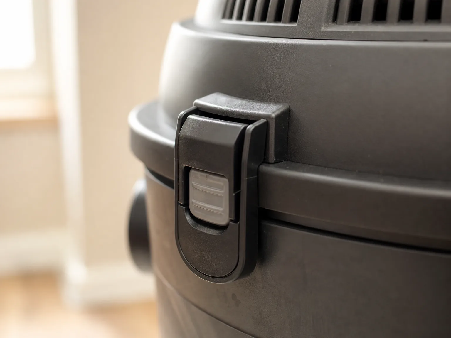 Close-up of the Vacmaster detachable blower latch mechanism on a wet/dry vacuum tank, warm natural light, soft cream background