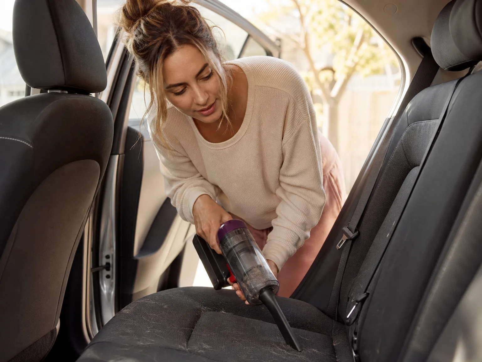 A woman using the ZARIMI handheld vacuum to clean pet hair from a car seat in natural morning light