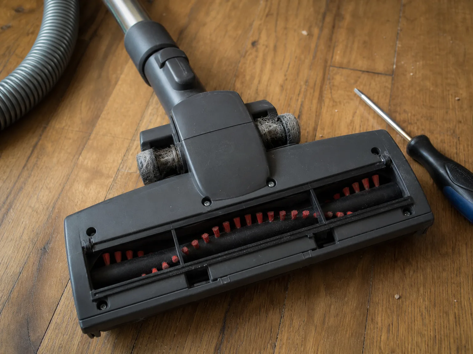 Close-up of a turbo brush head flipped over on a hardwood floor showing dog hair wound tightly around the screws beside the wheels