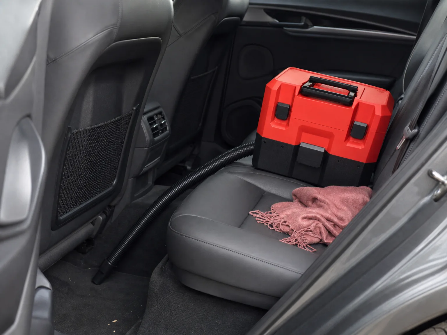 Compact cordless wet/dry vacuum sitting on a car seat with its short hose stretched taut down into the footwell